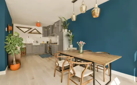 Un tavolo in legno con sedie in stile Wishbone, ideale per arredare sala da pranzo moderna. Parete blu intenso e cucina grigia completano l'ambiente.