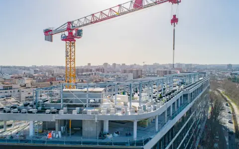 Grue de chantier sur un bâtiment en construction rapide, avec une ville en arrière-plan.