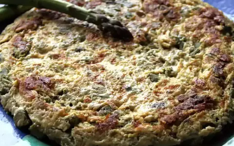 Tortilla de esparragos dorada y esponjosa, con espárragos frescos encima, servida en un plato azul.