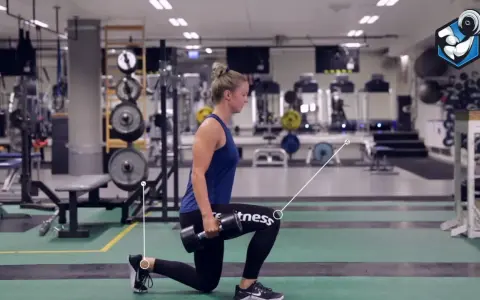 Kvinna utför utfallssteg med vikt i ett gym. Hon håller en hantel i ena handen och har ett ben framåt och ett bakåt.