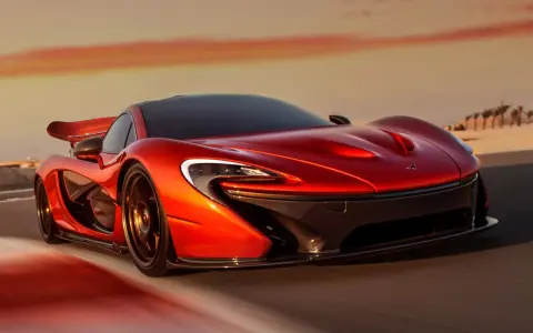Czerwony McLaren P1 pędzi po pustynnej drodze o zachodzie słońca.