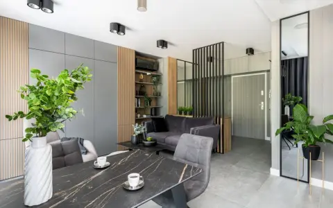 Nowoczesne mieszkanie 30m2 aranżacja: szara sofa, marmurowy stół, dużo zieleni i lustro.