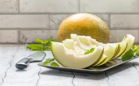 Kawałki melona na talerzu, obok cały owoc i nóż. Niska wartość melon indeks glikemiczny.
