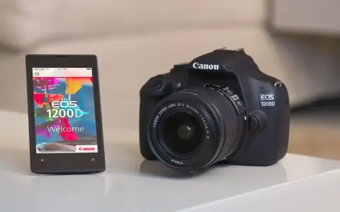 Czarny aparat cyfrowy Canon EOS 1200D obok smartfona z aplikacją powitalną.