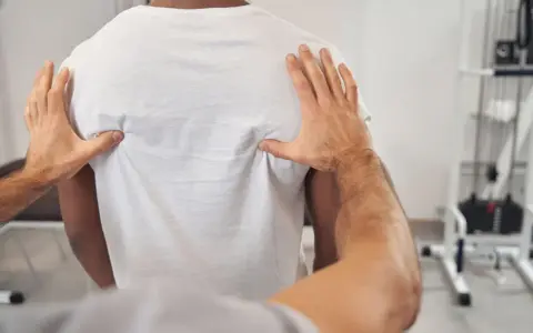 Fizjoterapeuta bada plecy pacjenta, oceniając kręgosłup piersiowy pod kątem objawów neurologicznych.
