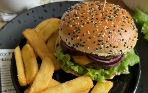 Soczysty burger wołowy z frytkami na czarnym talerzu.