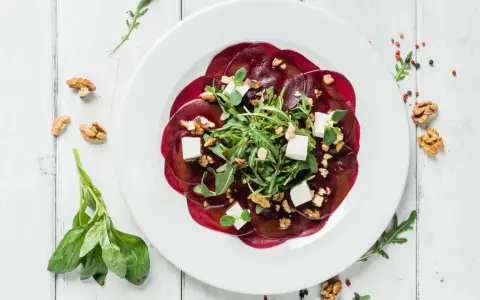 Rote Bete Carpaccio vegan mit Rucola, Walnüssen und veganem Feta auf weißem Teller.