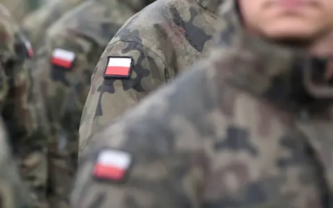Żołnierze w mundurach moro, z polskimi flagami na ramionach, czekają na swoją emeryturę wojskową.