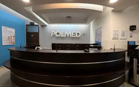 Recepcja kliniki medycznej POLMED z ciemnobrązowym ladą i logo na ścianie.