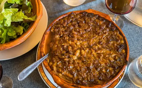 Cassoulet de Castelnaudary burbujeante en cazuela de barro, acompañado de ensalada verde y vino tinto.