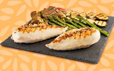 Dos jugosas pechugas de pollo a la parrilla, sazonadas con especias, acompañadas de espárragos, calabacín y champiñones.