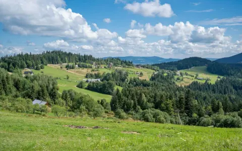 Zielone wzgórza Beskidu Wyspowego, pełne drzew i domków, pod błękitnym niebem z białymi chmurami.