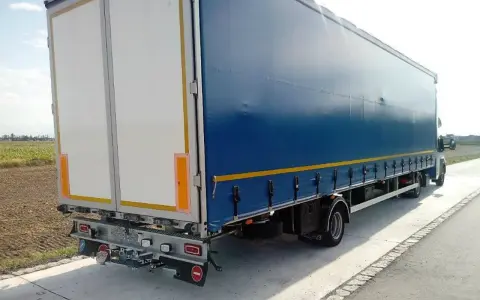 Ciągnik siodłowy z niebieską plandeką i białymi drzwiami naczepy, widok z tyłu i boku.