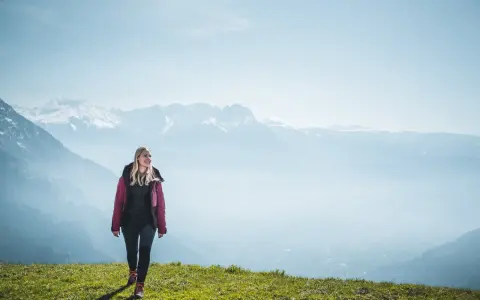 Frau in Wanderkleidung genießt die Aussicht auf verschneite Berge. Perfekt, was zieht man zum wandern an!