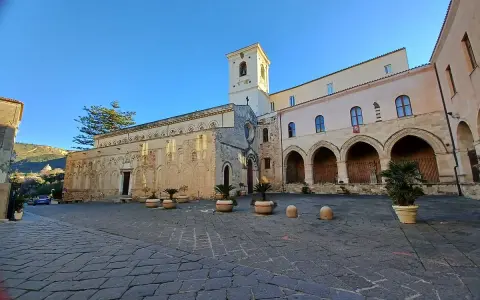 La piazza antistante la chiesa di Tropea, con il suo campanile e gli archi del chiostro, sotto un cielo azzurro.