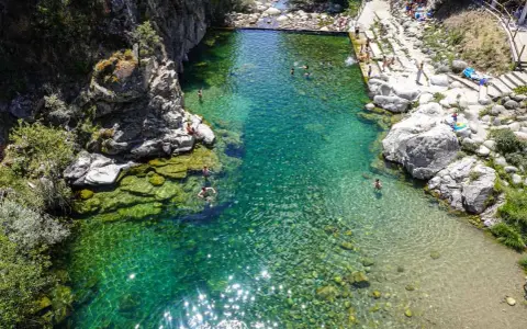 Una espectacular piscina natural en Extremadura, con aguas cristalinas y gente disfrutando del baño entre rocas y vegetación.