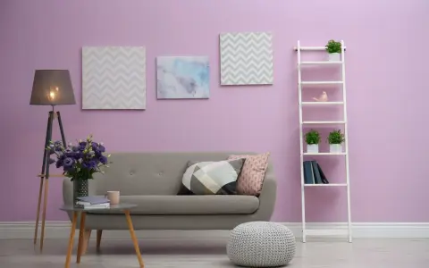 Przytulny salon z szarą kanapą, stolikiem kawowym z bukietem fioletowych kwiatów i dekoracjami na ścianie w kolorze liliowym.