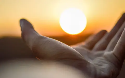 Dłoń otwarta ku słońcu, jak księga rodzaju, w blasku zachodu.