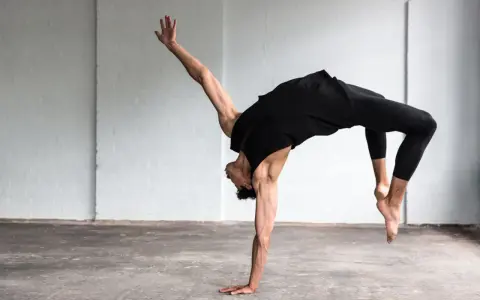 Un bailarín en un estudio blanco realiza un movimiento acrobático, mostrando que es la danza.