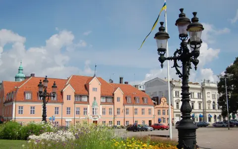Blumen blühen am Karlskrona Hafen. Ein prächtiges Gebäude mit orangem Dach und eine schwedische Flagge im Wind.