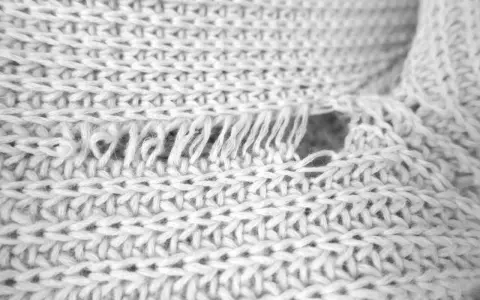 Nahaufnahme eines weißen Strickpullovers mit einem Loch und ausgefransten Fäden. Was tun, wenn die Wolle eingelaufen ist?
