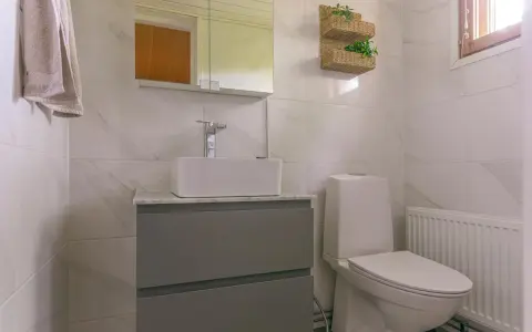 Modernt badrum med handfat och toalett utan avlopp. En handduk hänger på väggen.