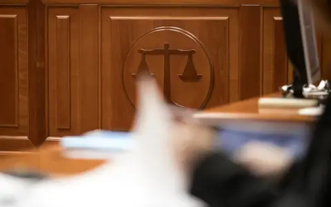 Drewniana ściana z symbolem wagi sprawiedliwości. Zastanawiasz się, ile czeka się na rozprawę w sądzie cywilnym? Czas oczekiwania bywa długi.