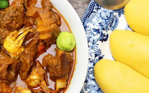 Un plat de foutou sauce graine avec de la viande et du crabe, accompagné de boules de pâte jaune sur une assiette décorée.
