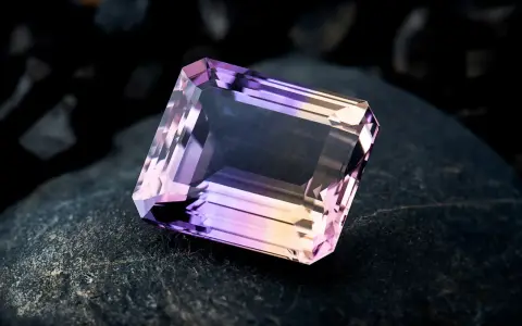 Un taglio a smeraldo sfaccettato mostra la transizione tra ametista e quarzo rosa, un connubio di colori su una roccia scura.