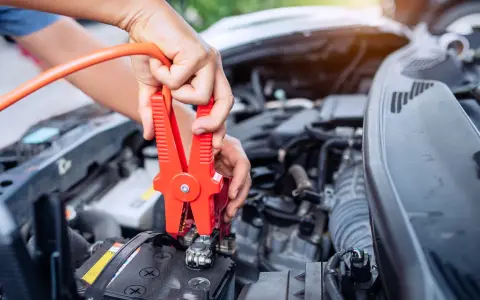 Hands connect jumper cables to a car battery, a common fix when wondering how long can a car be on before the battery dies.
