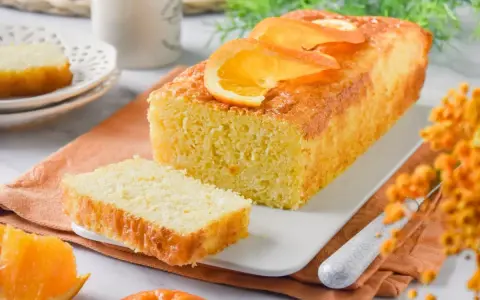 Un delicioso bizcocho de naranja, recién horneado y decorado con rodajas de naranja. Perfecto para acompañar un café.