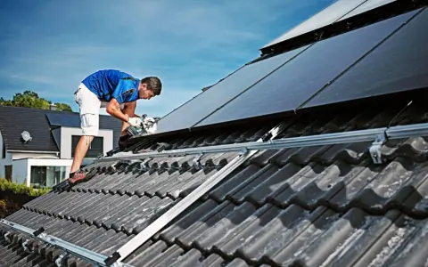 Handwerker montiert Solarmodule auf einem Dach. Dies geschieht unter Beachtung der hausanschluss strom vorschriften für eine sichere Installation.