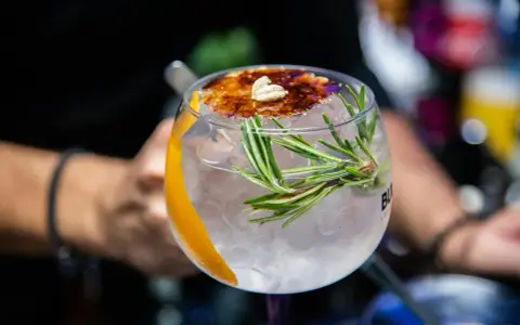 Ein erfrischender Gin Tonic, ein klassischer Cocktail, garniert mit Rosmarin, Orangenzeste und karamellisiertem Zucker.