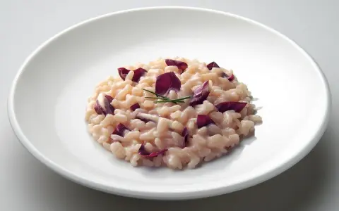 Un cremoso risotto al radicchio rosso, guarnito con erba cipollina, servito su un piatto bianco.