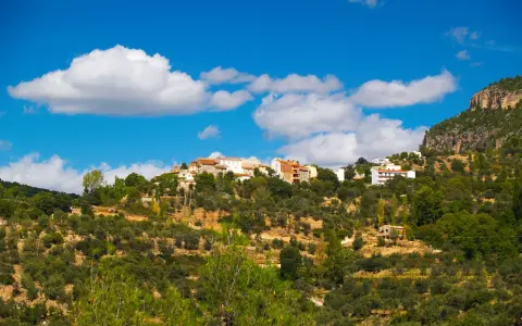 Pueblo blanco en la ladera de una montaña, rodeado de olivos y vegetación. El cielo azul con nubes blancas corona la vista de Gontar, Albacete.