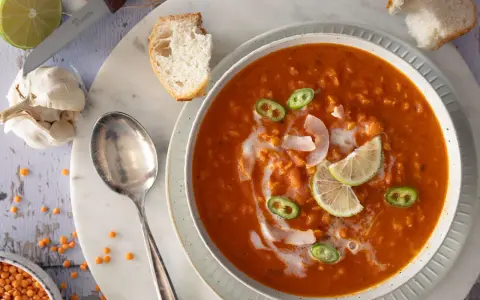 Eine cremige rote Linsensuppe mit Kokosmilch, garniert mit Limettenspalten und Jalapeños. Dazu gibt es knuspriges Brot.