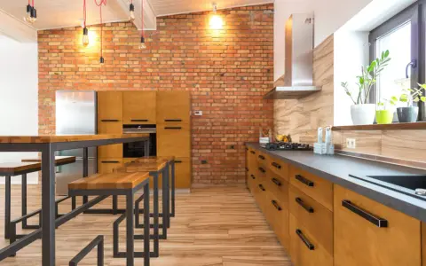 Cocina estilo industrial con paredes de ladrillo visto, muebles de madera y metal, y una isla con bancos.