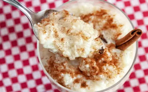 Cuchara con cremoso arroz con leche, espolvoreado con canela. ¿Quién inventó el arroz con leche? ¡Este postre es un clásico!
