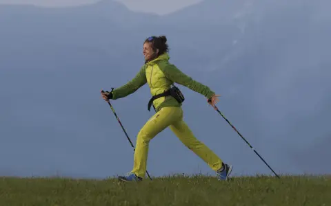 Donna sorridente pratica nordic walking su un prato. Informarsi sulle controindicazioni prima di iniziare.