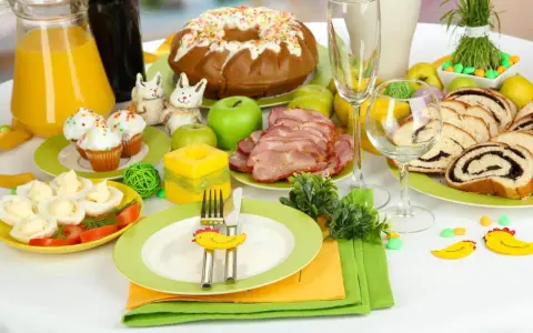 Stół z potrawami na święta wielkanocne: babeczki, jajka faszerowane, wędlina, makowiec, ciasto drożdżowe i sok.