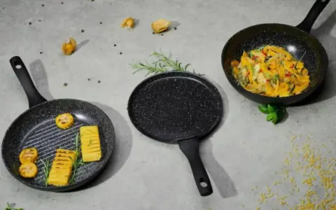 Trzy patelnie nie teflonowe: grillowa z polentą i kukurydzą, okrągła i woka z daniem warzywnym.