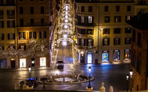 Roma di notte a Natale: una strada illuminata da luci scintillanti, negozi di lusso e una fontana. Un'atmosfera magica per scoprire cosa vedere a Roma a Natale.