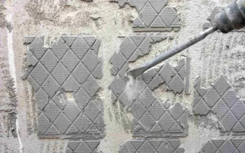 Outil de burinage en action pour enlever colle carrelage sur un mur en béton.