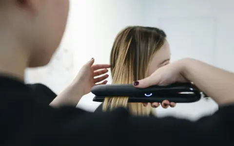 Stylist prostuje włosy po trwałej prostownicą.