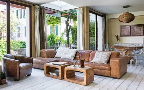 Accogliente soggiorno etnico chic con divano in pelle, poltrona vintage e vista sul verde.