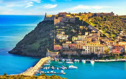 Incantevoli toscana paesaggi: un borgo colorato su una collina fortificata domina un porto con barche, baciato dal sole.
