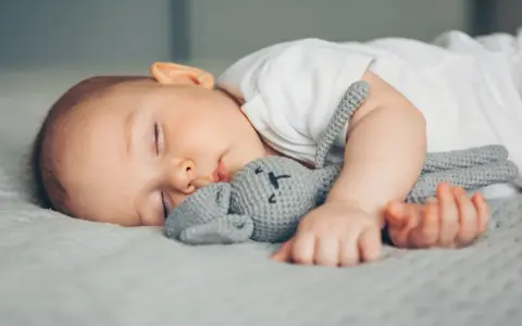 Ein Baby schläft friedlich mit seinem Häschen-Spielzeug. Vielleicht ist es die berüchtigte 4 monats schlafregression, die es so müde macht.