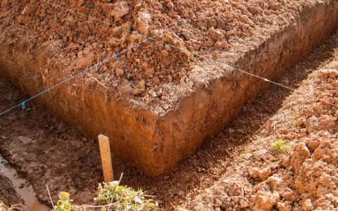 Wykonano wykop pod ławy fundamentowe. Widać ziemię, sznurki wyznaczające linie i drewniany palik.