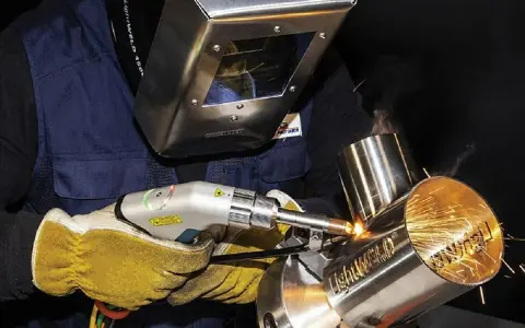 Operator w masce spawalniczej wykonuje napawanie laserowe metalowych elementów, tworząc iskrzące spoiny.