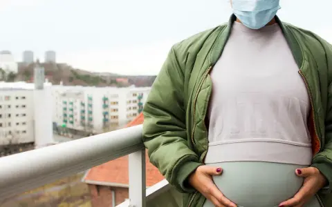 Gravid kvinna med munskydd på balkongen, omgiven av stadens silhuett. Känns det som att du är oftare sjuk gravid?